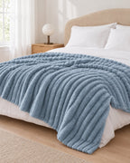 Plaid polaire côtelé Douillette, coloris bleu brume, sur un lit, chambre claire