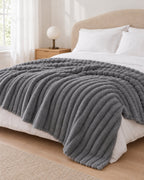 Plaid polaire côtelé Douillette, coloris gris anthracite, sur un lit, chambre claire