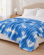 Plaid polaire côtelé Douillette, coloris tie-dye bleu ciel, sur un lit, chambre claire