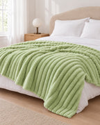 Plaid polaire côtelé Douillette, coloris vert sauge, sur un lit, chambre claire